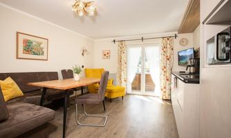A modern living room with a dining table and comfortable chairs. The large windows let in plenty of daylight and offer a view outside.
