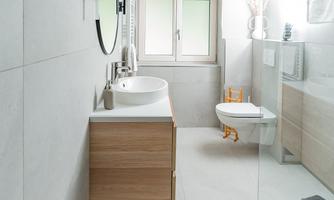 A modern bathroom with an elegant wooden dresser and a large mirror. The shower is open and the window lets in plenty of natural light.