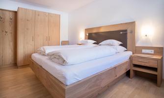 A modern bedroom with a large bed and light wood decor. There is a wardrobe and nightstands next to the bed.