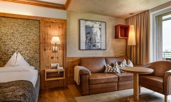 A cozy room with wooden decor, a comfortable sofa, and a small table. The large French door lets in a lot of light and offers a view outside.