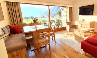 A cozy living and dining room with wooden floor. Large windows offer a view of the mountains and a green landscape.