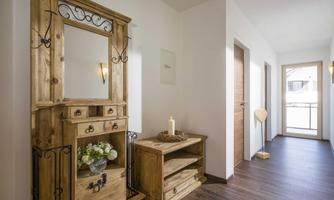 An inviting hallway with a wooden cabinet and a mirror. The walls are light and the floors are made of dark wood.
