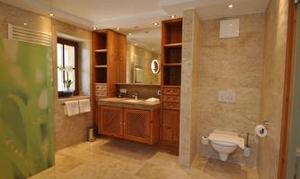 A modern bathroom with bright stone flooring and wooden cabinets. The room is well-lit and features a shower as well as a large sink with a mirror.