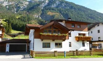 A charming house in a picturesque mountain landscape. The surroundings are green with tall mountains in the background.