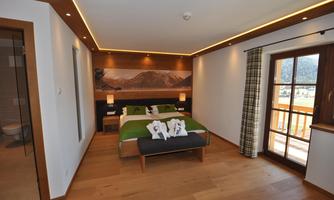 A modern furnished bedroom with a double bed and wooden floors. Large windows offer a view of the mountains and plenty of daylight.