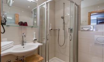 A modern bathroom with a glass shower and a sink. White tiles and wooden details give the space an inviting atmosphere.