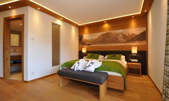 A modern bedroom with a double bed and a comfortable seating area. The walls are in warm wood and natural tones, complemented by soft lighting.