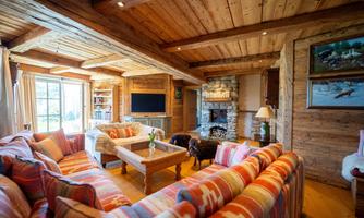 A cozy living room with wooden walls and a large window.  
Colorful sofas and a fireplace create an inviting atmosphere.