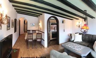 A cozy apartment with wooden beam ceiling and stylish furnishings. There is a living area with a sofa, a dining area, and an open kitchen.