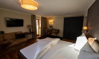 A modern hotel room with a comfortable bed, a sofa, and a desk. The room features large windows overlooking a balcony.