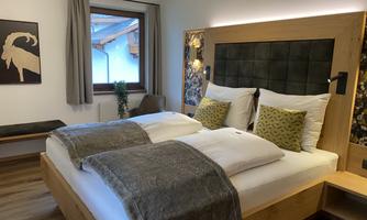 A cozy bedroom with a large double bed and modern wooden details. The windows let in plenty of natural light, and the decor is simple and stylish.