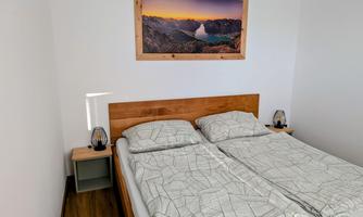 A bright bedroom with a double bed and modern design. On the wall hangs a picture of an impressive landscape.
