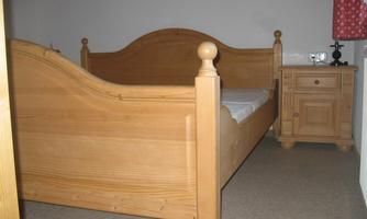 A simple bedroom with a wooden bed and a nightstand. The walls are painted in a neutral tone.