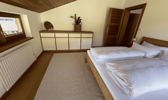 A cozy bedroom with a double bed and light wooden furniture. The windows offer a view of the surroundings and are equipped with modern decor.