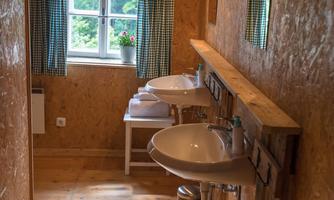 A bright bathroom with two sinks and wooden paneling. The window offers a view of nature outside.