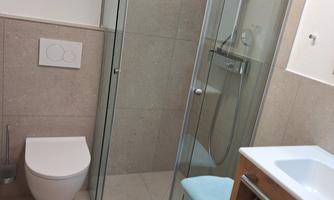 A modern bathroom with a shower and toilet. The walls are bright and made of stone, and there is a wooden vanity.