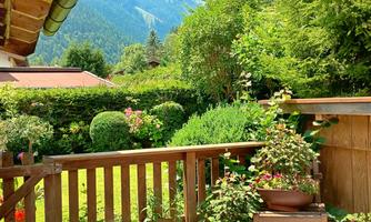 The patio is surrounded with a wooden fence that has a gate that can be closed with a hook. On the other side of the gate there is the main garden of the house with lots of flowers.