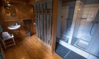 A cozy bathroom with wooden paneling. There is a sink and two showers in the corner.