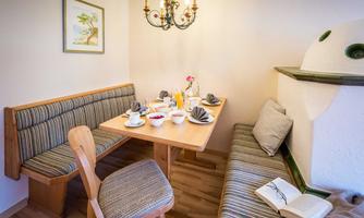 A cozy dining area with a wooden bench and a table set for breakfast. The table has plates, cups, and fresh fruit on it.