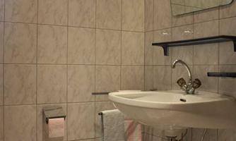 A small bathroom with tiled walls and a sink. There is a toilet and towels as well as a mirror.