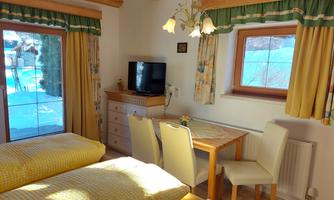 A cozy holiday apartment with wooden ceilings and large windows. The room is bright and tastefully furnished, with a dining area and a television.