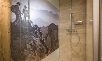 A modern bathroom with a glass shower cabin. On the wall, there is a picture of hikers in the mountains.