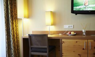 A modern hotel room with a desk, two lamps, and a television on the wall. A bowl of fruit is on the table.
