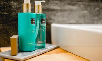 Two bottles of care products in a modern bathroom. A soap and shampoo bottle are placed on a wooden shelf next to a sink.
