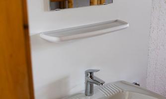 A modern sink with a mirror on the wall. In the background, a wooden bed is visible.