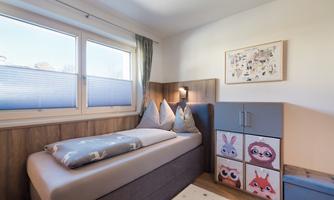 A cozy bedroom with a single bed and colorful boxes. Bright windows create a friendly atmosphere.