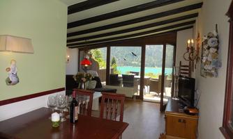 A cozy living space with a dining area, a view of the water, and large windows. The decor is stylish with wooden details and a pleasant atmosphere.