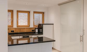 A modern kitchen with a black countertop and large windows. The walls are light and the cabinets have a minimalist design.