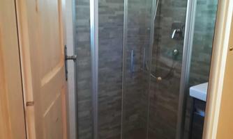 A modern shower with glass walls in a bright room. The floor is tiled, and there is a wooden door.