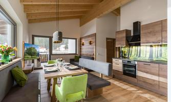 A modern dining room with a wooden ceiling and large windows. The table is beautifully set and there are cozy seating areas.