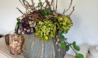 A beautiful floral arrangement in a decorative vase. The arrangement consists of green and purple plants as well as several branches.