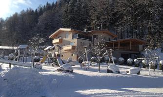 A beautiful house in the snow, surrounded by trees. The premises have playground equipment and a wintry landscape.