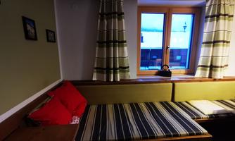 A cozy room with a window that opens up the view to the outside world. The bench is decorated with striped cushions and red accents.