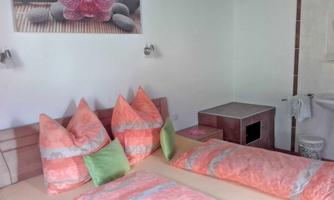 A cozy bedroom with a double bed and colorful pillows. A picture of an orchid hangs on the wall, and the room has a bright, inviting atmosphere.