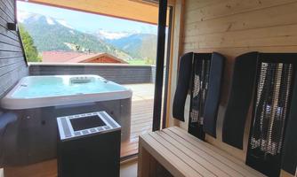A cozy room with a hot tub and a wooden bench. You can see the mountains through the window in the background.