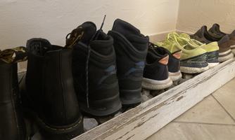 A row of shoes is standing in a wooden shelf. Below are boots and various sports shoes in different colors.