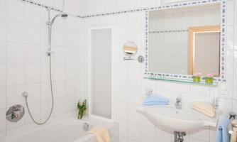A modern bathroom with a bathtub and a shower. The mirror and the sanitary facilities are clean and bright.