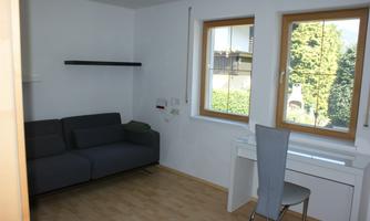 A simple room with a gray sofa and a desk. There are large windows that let in plenty of natural light.