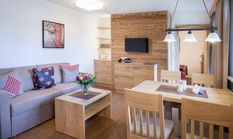 A modern living room with a cozy sofa and a wooden table. The room is bright and cheerful, featuring a dining table and a beautiful flower decoration.