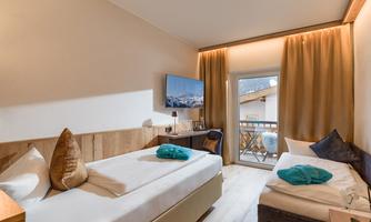 A cozy bedroom with two single beds and modern furnishings. The room has large windows with a view and is decorated in soft colors.