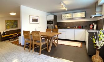 A modern kitchen with a wooden dining area. The space is bright and friendly, equipped with elegant furniture and a functional kitchen unit.