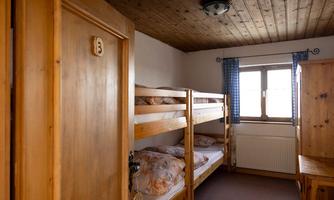 A simple room with two wooden bunk beds. There is a window with blue curtains and a wooden door.