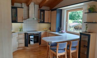 A modern kitchen with wooden ceilings and bright cabinets. There is a dining area with chairs and a large window overlooking the garden.