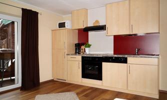 A modern kitchen with wooden cabinets and a red wall. The space is bright and cheerfully designed.
