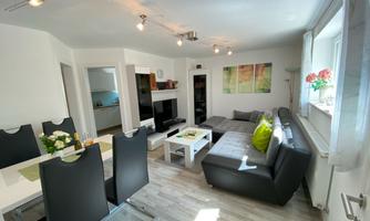 A modern living room with a cozy couch and a dining area. Large windows allow for plenty of natural light.