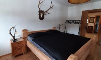 A cozy bedroom with a large wooden bed and black bedding. The room features rustic accents like antler decoration and a modern lampshade.